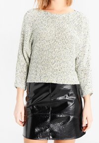 Maglione verde chiaro testurizzato con maniche a tre quarti abbinato a una mini gonna nera in ecopelle con dettaglio della cucitura frontale.