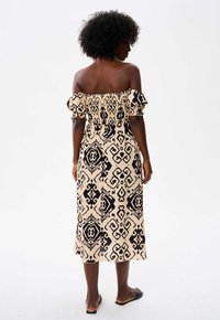 Off-shoulder jurk met een zwart-beige ikat patroon, pofmouwen, elastische lijf en een middellange A-lijn snit.