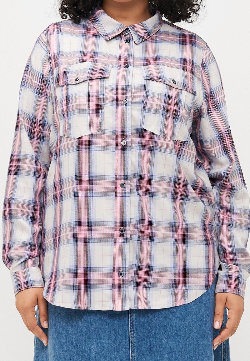 Chemise boutonnée à manches longues avec un motif à carreaux rose, bleu et blanc, dotée de deux poches poitrine à rabats, portée sur un jean bleu.