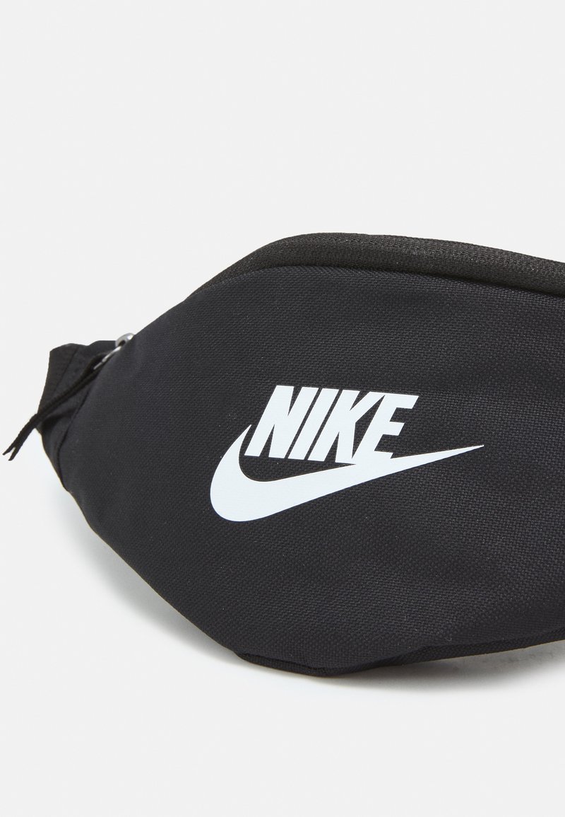 Riñonera negra de nailon con cierre de cremallera, que presenta un destacado logo blanco de Nike, forma curva y superficie texturizada.