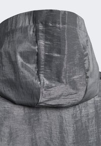 Šedý kapucňový oděv z pokrčeného, texturovaného materiálu. Má hladké švy a jemný lesk na povrchu látky.