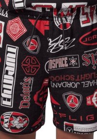 Pantaloni corti neri con un motivo ripetuto di loghi e grafiche bianche e rosse, inclusi marchi sportivi e simboli, con vita regolabile con cordoncino.