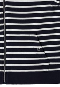 Gros plan sur un tissu rayé horizontal bleu marine et blanc avec une fermeture éclair à l’avant et une poche en biais avec un petit œillet en métal.