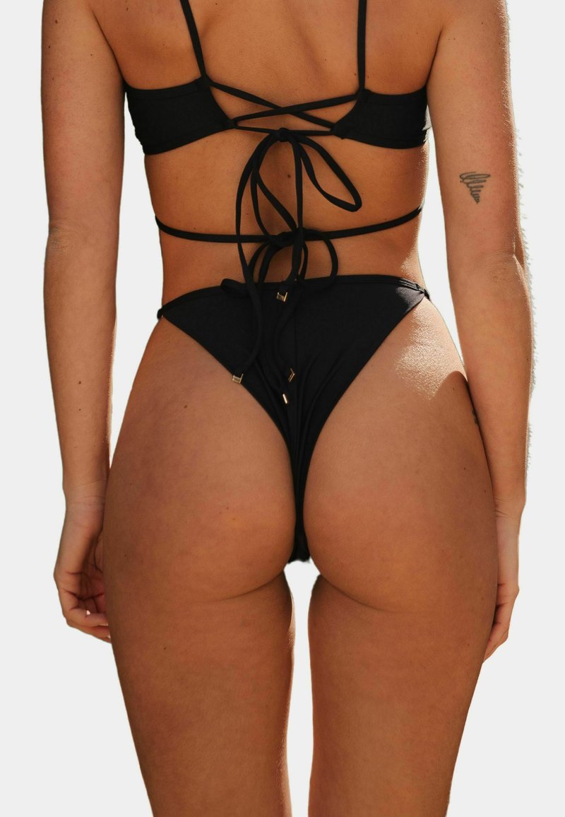 Czarny zestaw bikini z wiązanym tyłem, wysokimi majtkami i złotymi akcentami. Gładka faktura i minimalistyczny styl.