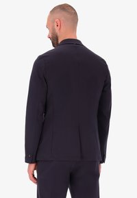 Blazer blu navy con un design su misura, maniche lunghe e uno spacco posteriore singolo. Realizzato in un tessuto liscio con polsini bottonati.