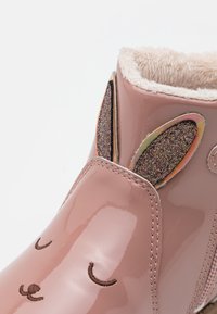 Růžová lesklá dětská bota s třpytivýma ušima králíčka a vyšívanýma zavřenýma očima a nosem, podšitá měkkou béžovou kožešinou.