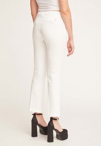 Pantaloni bianchi aderenti con gamba dritta e vita media. Presentano una tasca posteriore e un tessuto leggero e liscio. Abbinati a scarpe con tacco alto nere.