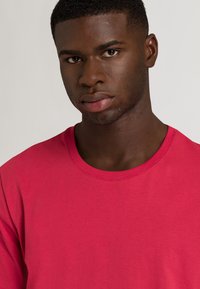 T-shirt a maniche corte di un brillante colore rosa, realizzata in cotone liscio. Presenta un classico collo a giro e una vestibilità rilassata, senza motivi o dettagli visibili.