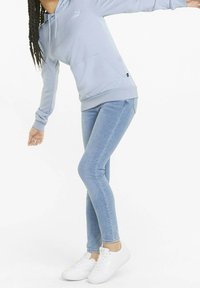Sudadera con capucha de color azul claro con bolsillo frontal, combinada con jeans ajustados de color azul claro y zapatillas blancas. Tejido suave y diseño casual.