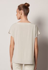 Ljust beige kortärmad topp med vid halsringning och slät yta. Har en avslappnad passform och subtila sidslitsar vid fållen.