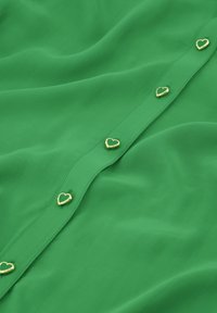 Groene shirt van een gladde stof met een knoopsluiting aan de voorkant. Opvallende gouden hartvormige knopen verbeteren het ontwerp.