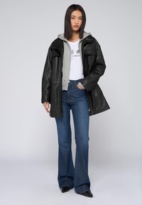 Czarna skórzana kurtka na szarej bluzie z kapturem, biała koszulka z grafiką i niebieskie dzwony. Całość dopełniają czarne, spiczaste buty.