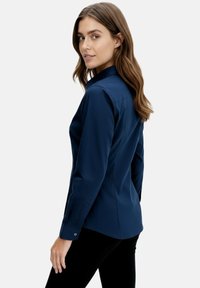 Navy long-sleeve shirt with a collar, button cuffs, and a fitted design. Smooth fabric, minimalistic with no visible patterns or accents.