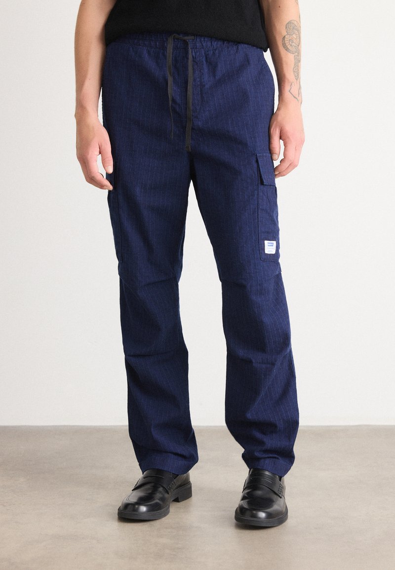 Navy blue cargo pants with pinstripe pattern, elastic waistband, black drawstring, and side pockets. Worn with black leather shoes.