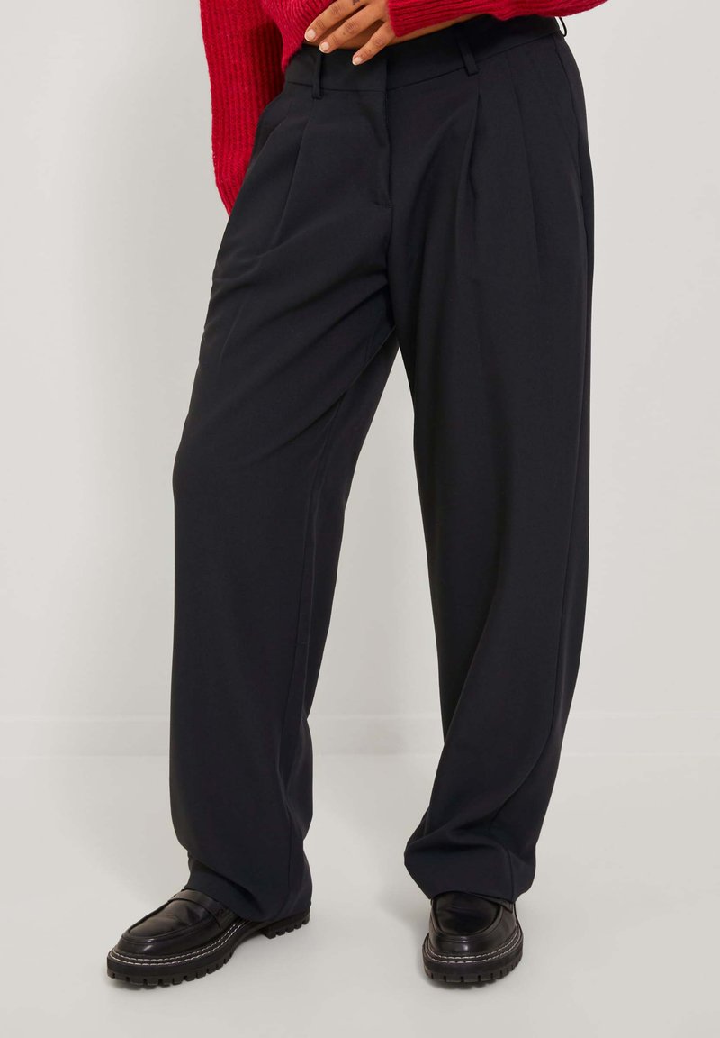 Svarta plisserade byxor med en lös passform. Tillverkade av ett mjukt tyg, med hög midja och sidofickor. Matchat med svarta skor.