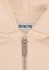 Felpa con zip di colore beige chiaro con una texture liscia, zip in metallo e un'etichetta con la scritta "DISTRETTO". Il design include un cappuccio e bordi a costine.
