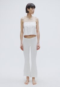 Haut court blanc à fines bretelles, texture détaillée. Pantalon blanc évasé ajusté, tissu lisse, sans motifs, porté pieds nus.