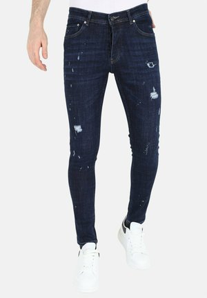 Skinny-fit donkerblauwe jeans van denim, met versleten details en verfspetters. Gecombineerd met witte sneakers.
