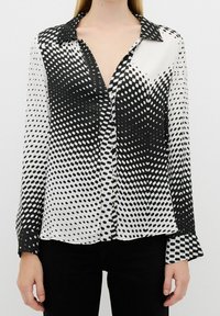 Black and white polka dot blouse with a silky texture, featuring a collar, button front, and long sleeves with flared cuffs.
