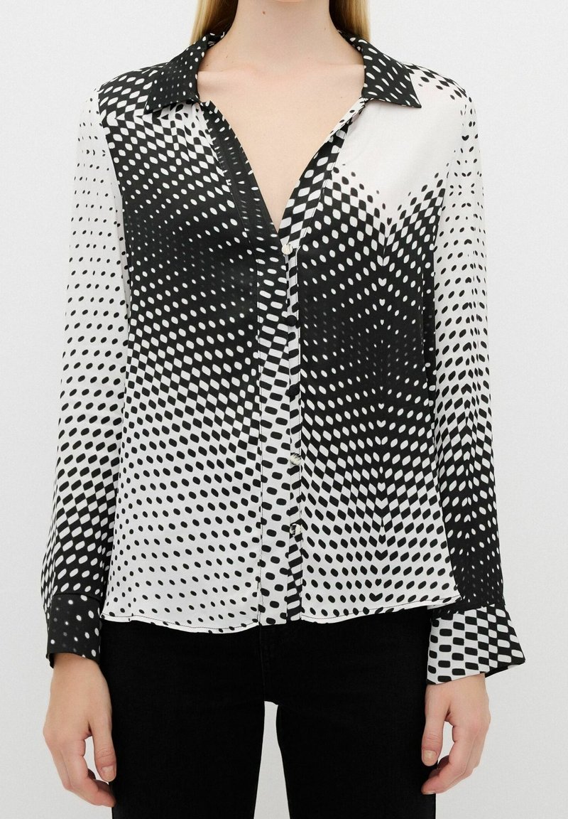 Black and white polka dot blouse with a silky texture, featuring a collar, button front, and long sleeves with flared cuffs.