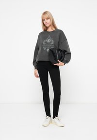 Grijze oversized sweatshirt met grafisch ontwerp, gecombineerd met zwarte legging en witte sneakers, met een gladde textuur en een comfortabele pasvorm.