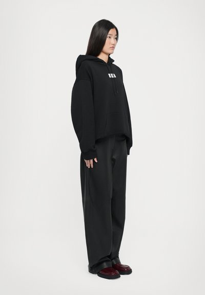Svart oversize hoodie med en framficka och dragsnodd, matchat med löst sittande svarta byxor och vinröda skor.