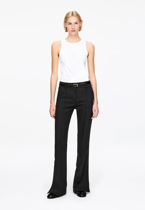 Black tailored pants with a straight leg, featuring a sleek belt. Paired with a fitted white tank top. Minimalist design and clean lines.