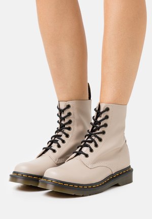 Stivaletti beige allacciati realizzati in pelle liscia, con lacci neri, cuciture a contrasto e una suola in gomma robusta con finitura gialla.