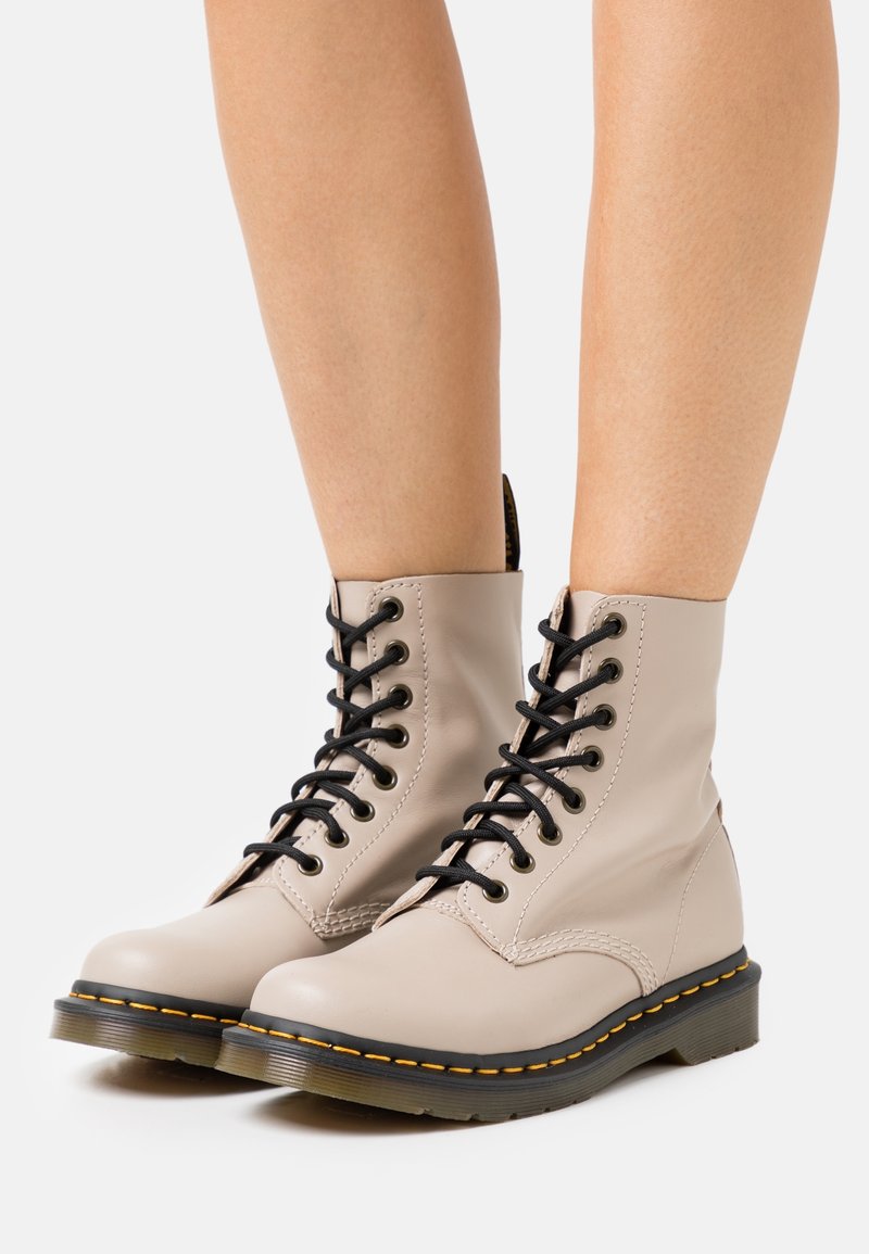 Botines beige con cordones, hechos de cuero suave, que cuentan con cordones negros, costuras de contraste y una suela de goma resistente con ribete amarillo.