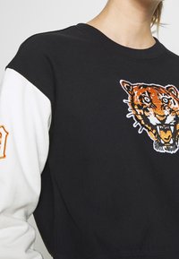 Felpa bianca e nera con ricamo di una tigre arancione e nera. Il design presenta una texture a coste e una vestibilità rilassata.