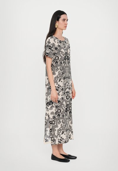 Il vestito presenta un motivo paisley floreale bianco e nero, maniche corte, scollo rotondo e una vestibilità lunga e ampia. Indossato con scarpe flat nere.