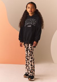 Svart hoodie med texten "PARIS 1982" i vitt; kombinerad med kremfärgade vida byxor med leopardmönster; svarta sneakers med beige sulor.