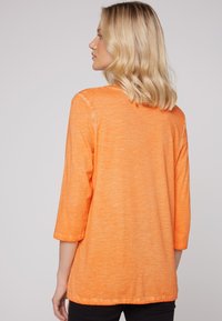 Oranges T-Shirt mit langen Ärmeln und lockerer Passform, ausgestattet mit einem runden Halsausschnitt und weichem, texturiertem Stoff. Lässiges Design, ideal für den Alltag.