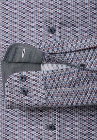 Langemouwen shirt met opgerolde manchet, geometrisch hexagoonpatroon in blauw, rood en wit, met zwarte knopen op de manchet en aan de voorkant van het shirt.