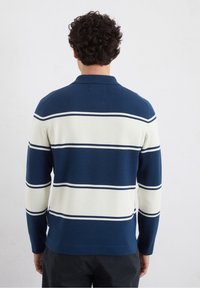 Maglione polo lavorato a maglia con strisce blu navy e crema, dotato di colletto e maniche lunghe, realizzato in un morbido tessuto con una finitura texturizzata.