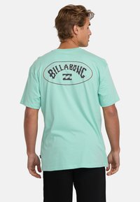 Mint green short-sleeve t-shirt made of cotton, featuring a bold "Billabong" logo on the back with a wave design in black outline.