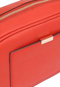 Rode leren clutch met een gladde textuur, voorzien van een gouden rits en een rechthoekige buitenzak. Minimalistisch ontwerp met een metallic accent.