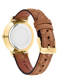Goldfarbene Uhr mit einem Gehäuseboden aus Edelstahl, braunem Lederarmband mit geprägten Mustern und einer gebogenen Schnallenverschlus.