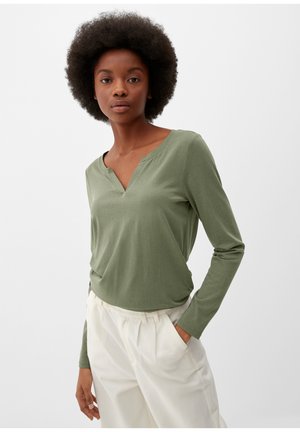 Long-sleeve, olive green top with a V-neckline and a relaxed fit, made of soft fabric, paired with cream trousers.