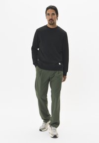 Zwarte sweatshirt van structuurstof, met ronde hals en geribde boorden. Gecombineerd met lichtgroene broek en beige sneakers met grijze accenten.