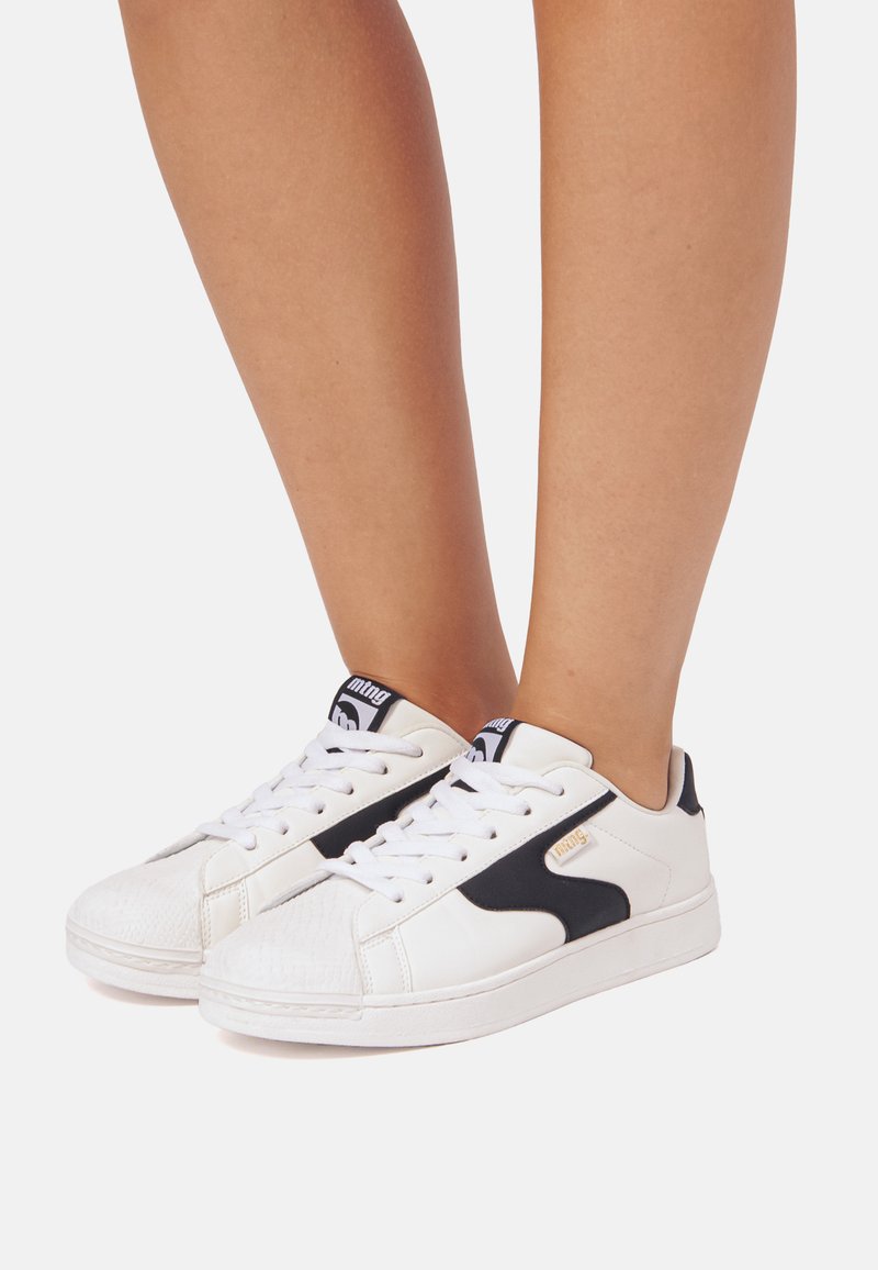 Sneaker bianche con accenti neri, punta testurizzata e lacci piatti. Presentano una linguetta con marchio e dettagli del logo laterale.