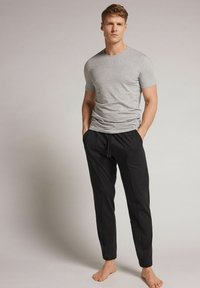 Grijze short-sleeve t-shirt gedragen met zwarte tapered joggers met een trekkoord in de taille en zijnaden, weergegeven op een effen achtergrond.