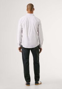 Camisa de rayas para hombre en tonos claros y oscuros, de manga larga, con puños abotonados, corte relajado, combinada con jeans oscuros y calzado casual.