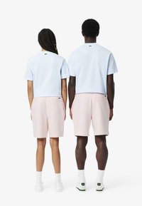 T-shirt in cotone azzurro chiaro e pantaloni corti rosa, con un dettaglio del logo sul retro. Entrambi gli outfit presentano una vestibilità rilassata e una texture del tessuto morbida.