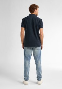 Polo de marină din țesătură texturată, cu mâneci scurte și guler, asortat cu blugi albaștri deschis și adidași crem.