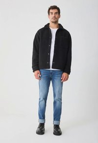 Giacca in pile nera con chiusura a bottoni e taschino sul petto, abbinata a jeans azzurri con risvolti e stivaletti neri alla caviglia.