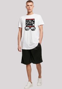 White cotton t-shirt with black and red "RUN DMC" graphic and glasses print, paired with black shorts and white sneakers.