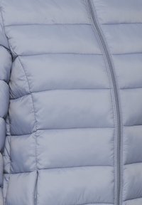 Doudoune bleu clair avec une texture matelassée, des coutures verticales et une fermeture éclair avant. Elle possède une finition lisse et brillante ainsi que des poches latérales.