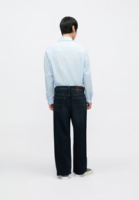 Világoskék gombos ing hosszú ujjakkal, sötétkék széles szárú farmerral párosítva; látható hátsó zsebek és márkajelzés a derékrészen.