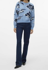 Světle modrý pletený svetr s květinovým vzorem v tmavě modré a krémové barvě, spárovaný s tmavými džíny a špičatými černými botami.